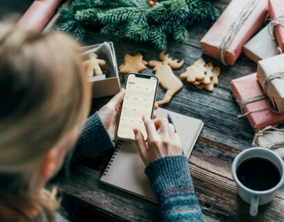 Woman planning holding a phone with a calendar on the screen working on christmas desk