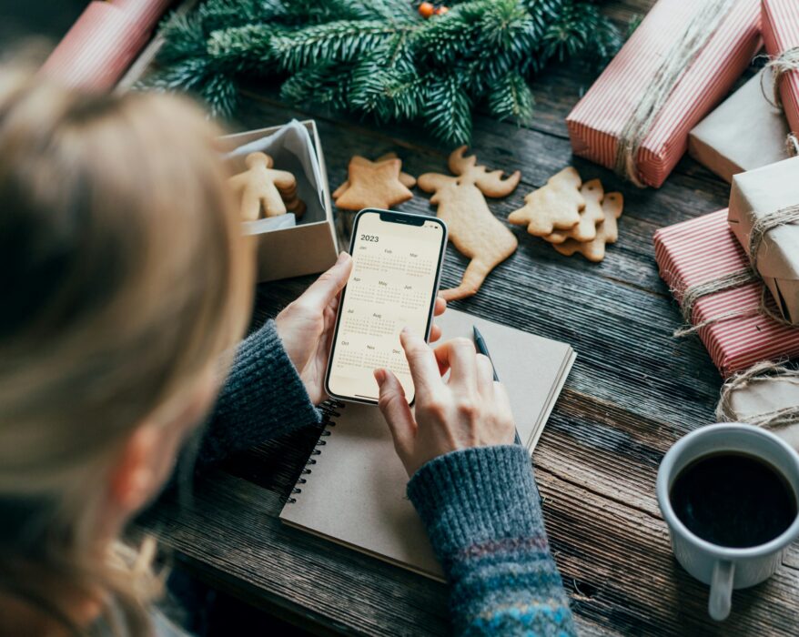 Woman planning holding a phone with a calendar on the screen working on christmas desk