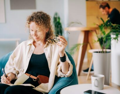 Woman puts on glasses and writes in paper notebook