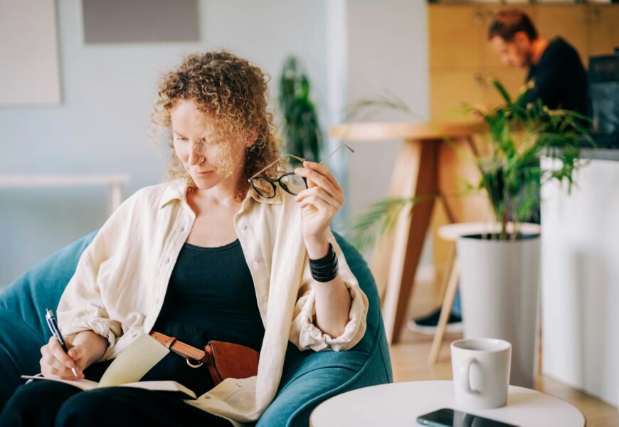 Woman puts on glasses and writes in paper notebook